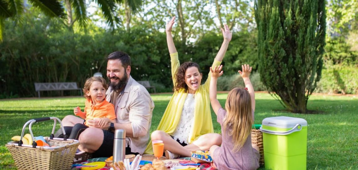 Happy family enjoying a sunny picnic with children on a blanket in a Portugal park.